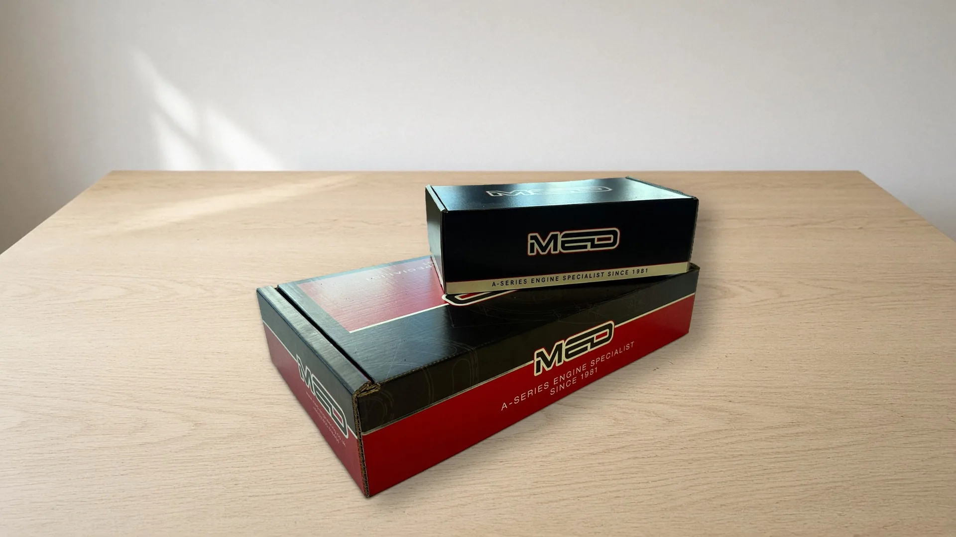 Two printed MED mailer boxes, red and black, stacked on a light wooden table